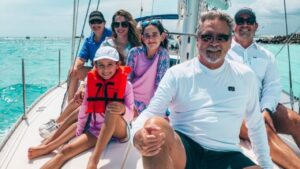 A smiling family sitting on a sailboat deck during a sunny day at sea