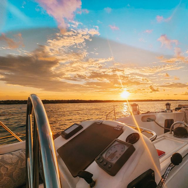View from a sailboat at sunset with golden light reflecting on the water.